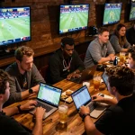 Intensely focused friends enjoying sports betting at https://xoilac.now/ with live match screens in the background.